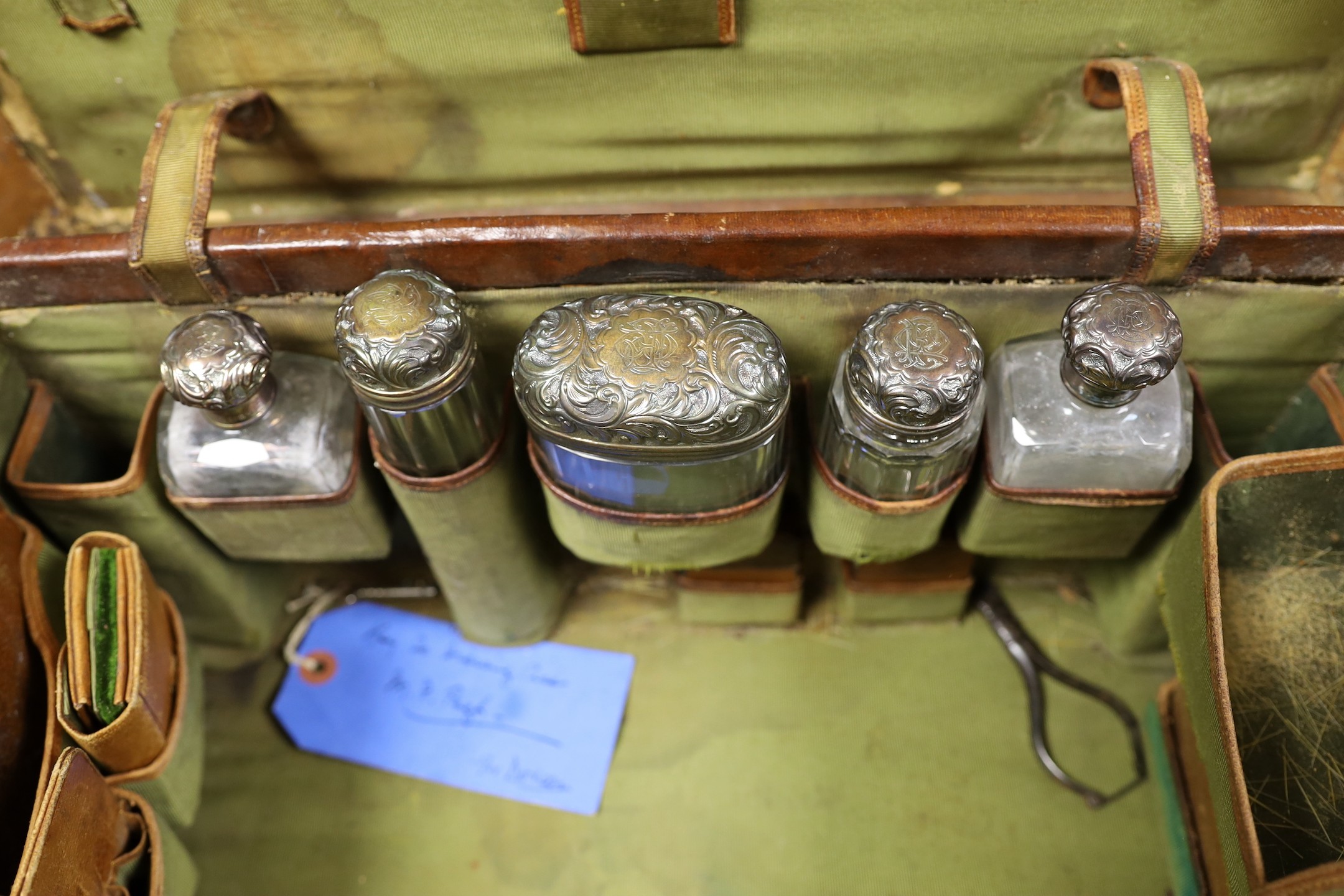 A late Victorian leather travelling vanity case containing five repousse silver topped glass toilet jars, 43.8cm.